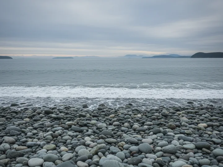 A smooth cobblestone beach under soft grey light, still water reaching to the horizon.